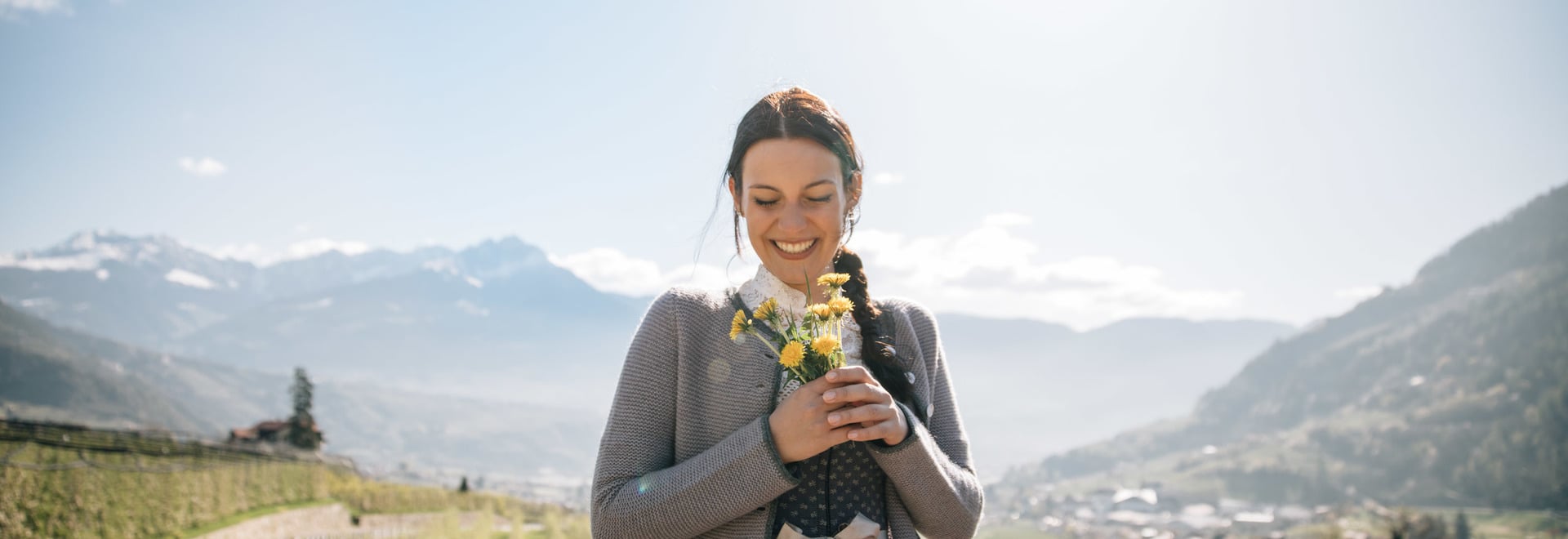 Frau in Tracht hält Blumenstrauß vor Algunder Panorama